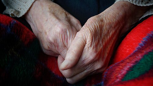 An elderly person's hands clasped together over a blanket