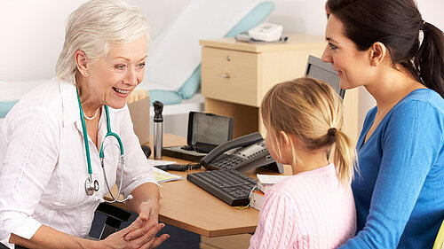 A mother holding a child whilst speaking to a GP
